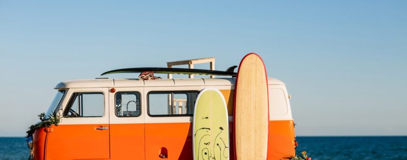 bus with a surfboard on the roof is a parked near the beach.